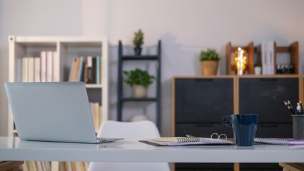 Simple workspace with laptop, notebooks, coffee cup and pencil holder on white table.