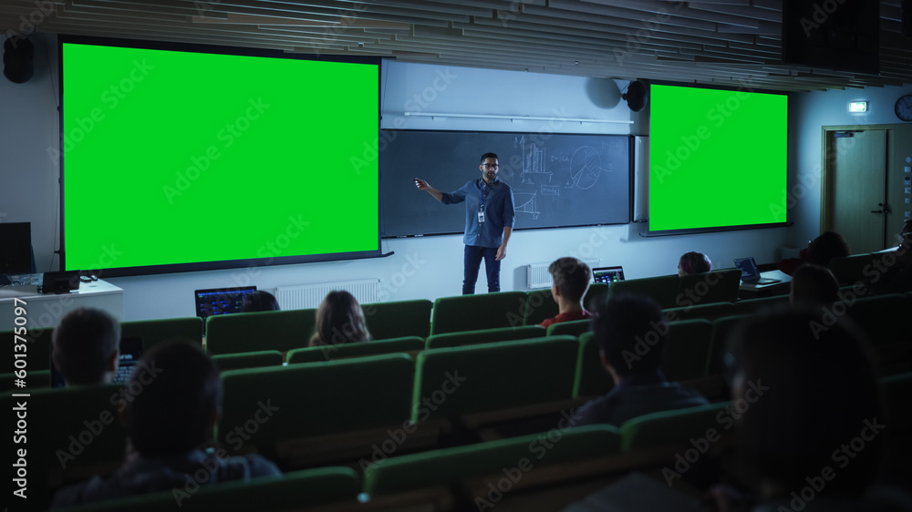 Aufkleber Young Male Teacher Giving a Lecture, Showing Slides on a Green Screen Mock Up Display to a Diverse Multiethnic Group of Female and Male Students in Dark College Auditorium