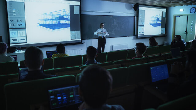 Young University Professor Explaining an Interior Design Styles Lecture to a Group of Diverse Multiethnic Students in a Dark Auditorium. Female Teacher Showing a Housing Project on Two Big Screens