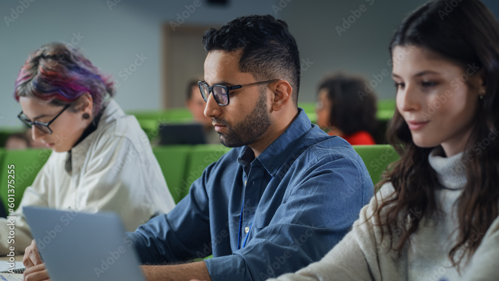 Poster Young Handsome Male Student Studying in University with Diverse Multiethnic Classmates. Young Man is Writing Down Lecture Summary in Notebook to Prepare for College Exams