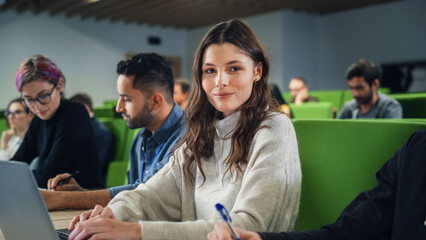 Beautiful Smart Female Student Studying in University with Diverse Multiethnic Classmates. Portrait of a Happy Caucasian Female Looking at Camera and Smiling. She is Using a Laptop Computer
