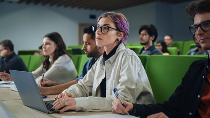 Smart Creative Female Student Studying in University with Diverse Multiethnic Classmates. Young Woman with Colored Short Hair is Using a Laptop Computer. Taking Notes from a Lecture in College