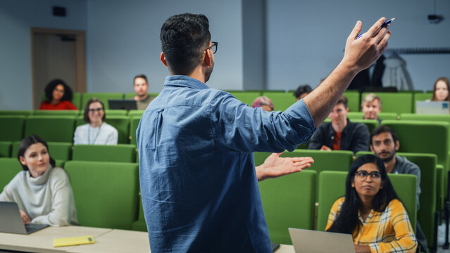 Male Teacher Giving a Lecture to a Diverse Multiethnic Group of Female and Male Students in Modern College Room. Curious and Thoughtful Scholars Studying and Listening to Lecturer. Camera Facing Class - Powered by Adobe