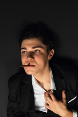 Close-up portrait. Lying on a floor Young mafia member with a slicked back hair, dressed in black suit smoking a cigar. Defeated, Dying shot Italian mafia gangster. isolated on black background.