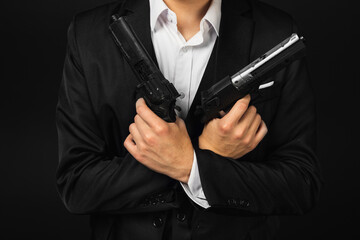 A man in black suit with crossed arms hold two guns or pistols in hands. Italian mafia gangster. isolated on black. unreconizable, no face.