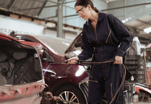 Woman welder welding damaged body car with blue spark at workshop. Female auto mechanic working at repair garage fixing broken vehicle with skill. Women worker in automotive maintenance industry.