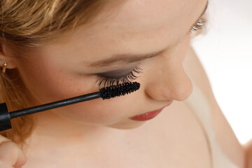 closeup of a young woman applying mascara on a white background