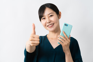 スマートフォンを持ちながらグッドサインをする若い女性