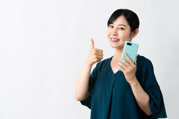 スマートフォンを持ちながらグッドサインをする若い女性