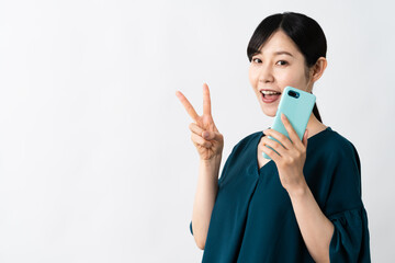 スマートフォンを持ちながらピースサインをする若い女性
