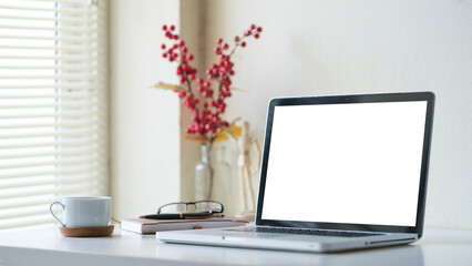 Bright home office interior with laptop, coffee cup, books and glasses on white table.