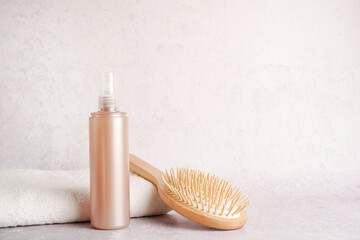 Still life with shampoo or lotion bottle and wooden hair brush with white towel on light concrete...
