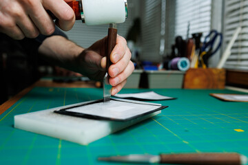 Hands of a professional craftsman make a leather wallet new, clean genuine leather wallet, close-up cropped shot.