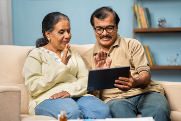 Indian senior couple talking with doctor on video call using digital tablet at home - concept of online consultation, medicare and home health care