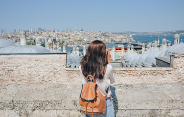 Fototapeta na wymiar A young traveler with a backpack on her back looks at the landscape from the Suleymaniye Mosque on a sunny day in Istanbul.