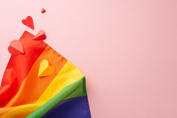 A top-down view of LGBT History Month arrangement idea with rainbow flag and colorful hearts, on a pastel pink background, and a blank space for text or promotional purposes