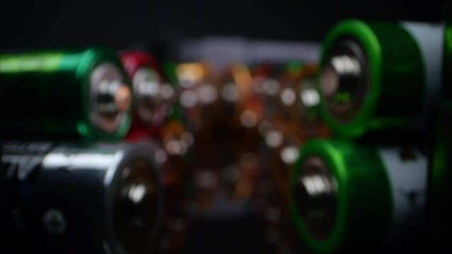 Camera focuses on discarded alkaline batteries, often used in portable electronics. Filmed in macro on a dark surface.