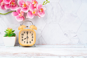 The Wooden alarm clock and pink color orchid on wooden floor with copy space for your design.