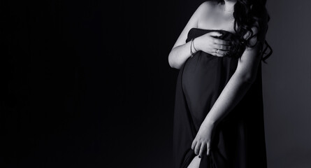 pregnancy woman in a black dress on a black background with copy space, studio pregnancy photo shoot