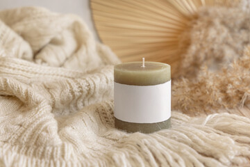 Obraz na płótnie Canvas Candle with label on cosy sweater near dry pampas grass and palm leaf, Close up, mock up