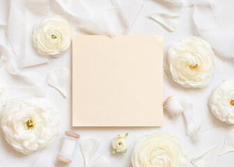 Fototapeta na wymiar Square blank card near cream roses and white silk ribbons top view, wedding mockup