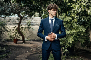 Handsome male model in blue suit standing over blured garden