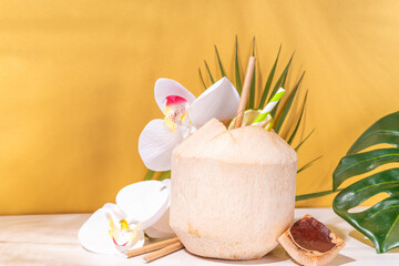  Young Thai coconut cocktail or juice, tropical summer drink in whole young coconut, with tropical leaves, decor and flowers, on high-colored background 