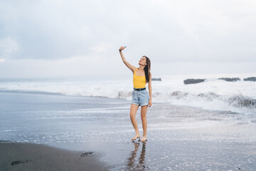Happy woman shooting selfie with smartphone on sandy beach