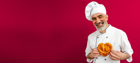 Baker man in love on valentine's day wearing chef's outfit. Chef-cooker in a chef's hat and jacket holding a heart-shaped muffin to his chest. Senior Character kitchener, pastry chef for advertising