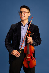 Portrait with handsome, young musicians, violinist wearing elegant suit and eyeglasses holding...