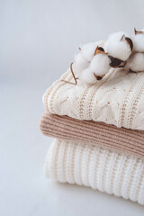 Fototapeta na wymiar Stack of knitted sweaters with cotton flowers on white background.