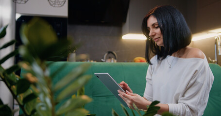 Good looking of young caucasian woman in casual clothes is using a digital tablet and smiling while sitting on couch at home