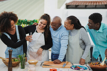 Happy african family having fun looking on smartphone while cooking dinner outdoor at home patio