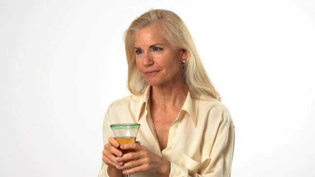 Closeup portrait of beautiful smiling happy blond mature woman holding wineglass and drinking wine looking to the side on solid white background with copy space