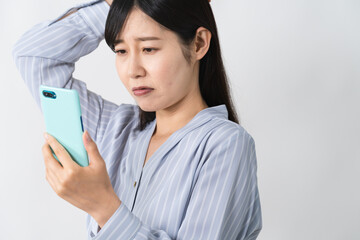 スマートフォンを持ちながら頭を抱える若い女性