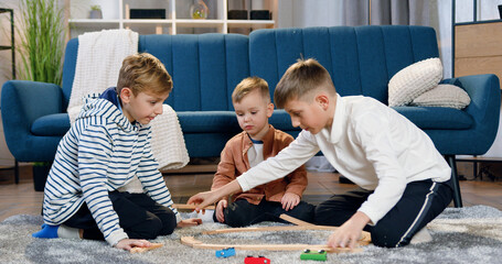 Adorable friendly different ages three brothers having fun together when gathering car track on the...