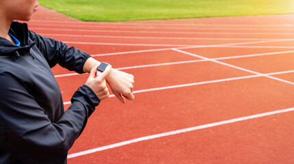 Woman athlete runner standing on running tracks and using her digital wrist watch.