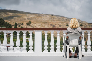 Greece vacation enjoyment, adult traveling woman sitting in patio on chair and admiring the old city, travel through Greek islands of the Dodecanese archipelago, famous vacation and travel destination