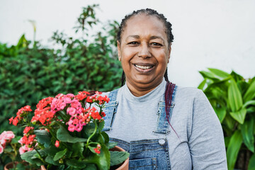 Happy african senior woman smiling on camera while holding flowers at home terrace - Gardening...