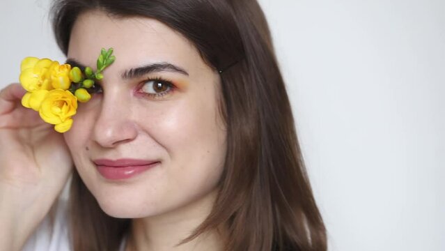 Young beautiful woman with creative colorful make up posing with yellow freesia flower