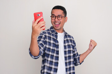 Adult Asian man clenched fist showing excited when looking to his mobile phone