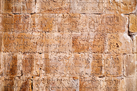 The Georgian alphabet is carved on the stone wall of an ancient temple in the Ananuri fortress. Texture background of ancient temple wall