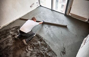 Top view of male construction worker placing screed rail on the floor covered with sand-cement mix....