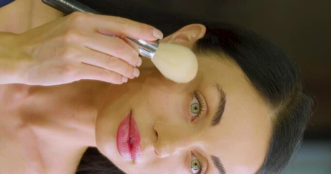 Young Caucasian woman applying makeup in fromt of mirror at home.