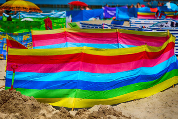 Parasol słoneczny na plaży nadmorskiej w wakacje razem z parawanem na wiatr.