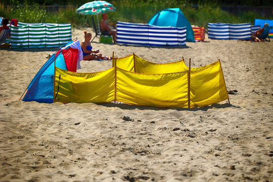 Parasol słoneczny na plaży nadmorskiej w wakacje razem z parawanem na wiatr.