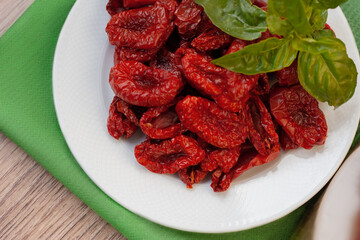A plate of sun-dried tomatoes on a wooden background, basil, green napkin, top view
