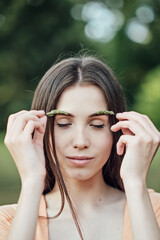 Natural Eyebrows cosmetics, eyebrow makeup and care trends. Candid portrait of young woman holding green plants herbs near eyelashes