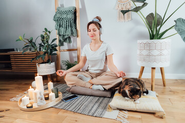Young healthy woman practicing meditation at home, wearing headset, sitting in lotus position on...