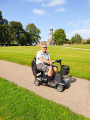 Disabled man enjoys the freedom to get out and about on his disability scooter, riding through the park in Shrewsbury on a sunny summers day.
